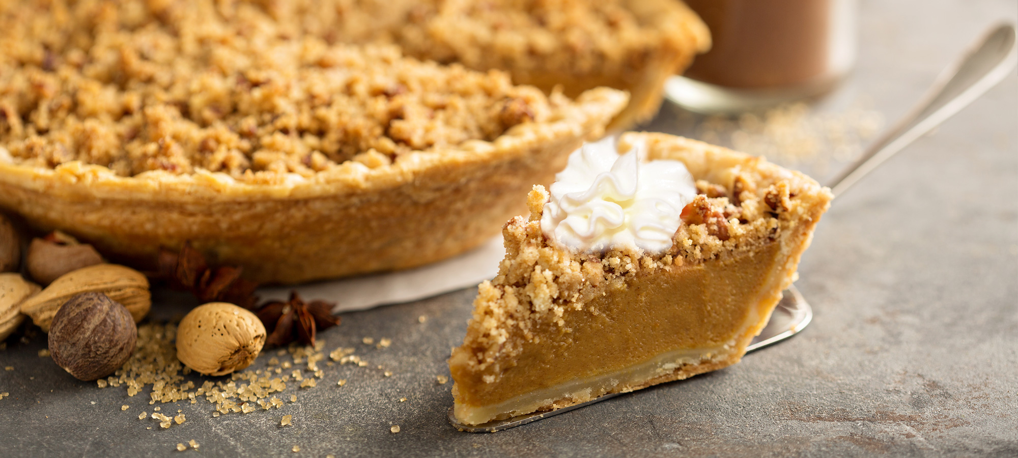 A slice-view of a Caramel Pumpkin Pie With Pecan Streusel and Bourbon Brown Sugar Whipped Cream.