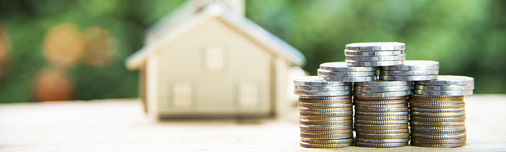 Stacks of coins in the foreground with blurred model house in the background.