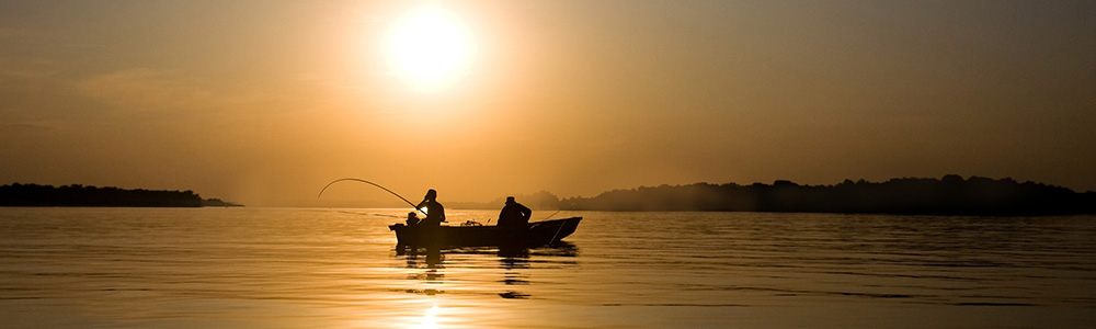 Boaters fishing on a lake at sunrise.