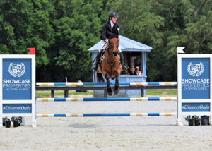 A horse and rider jumping over a Showcase Properties jump at Florida Horse Park.