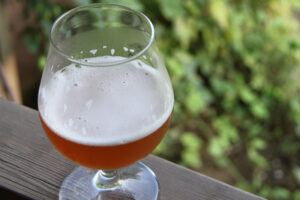 A glass of beer on a wooden deck railing.