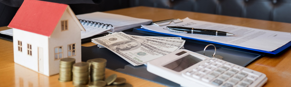 A model of a home, a stack of money, a calculator, and financial paperwork