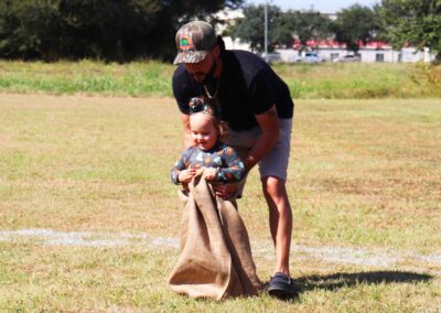 A man helping a little girl during a potato sack race.