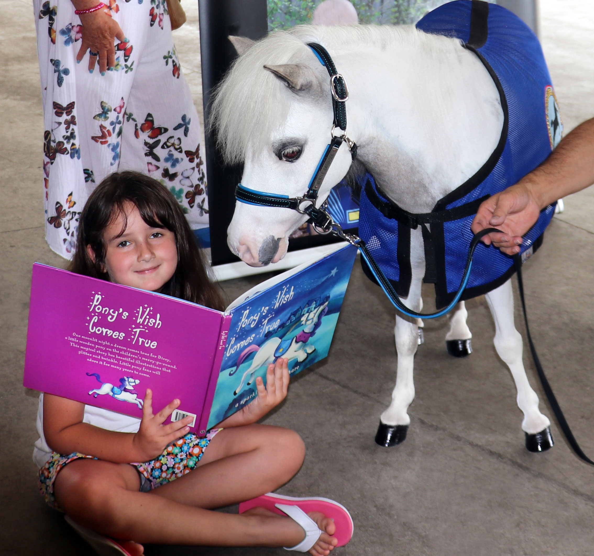 A miniature horse and a young girl share a book.