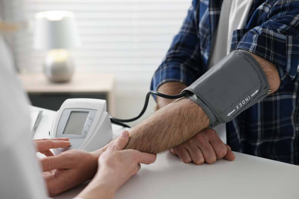 Doctor measuring blood pressure of man at table indoors, closeup Doctor measuring blood pressure of man at table indoors, closeup